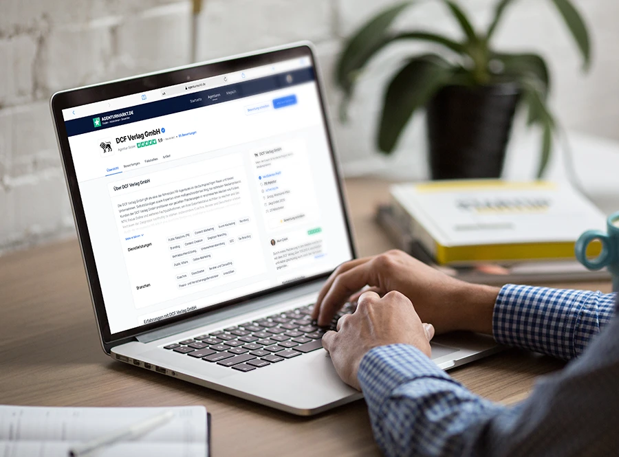 Person recherchiert DCF Verlag GmbH auf Agenturmarkt.de – Profilseite einer Agentur mit Bewertungen auf Laptop